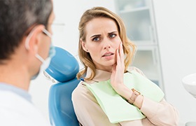 Woman in dental chair holding cheek during emergency dentistry