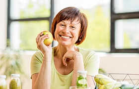 Woman with dental implant replacement teeth eating a green apple