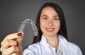 Woman holding up Invisalign clear aligner tray