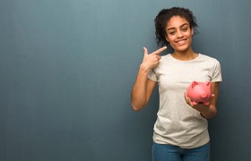 woman holding a pink piggy bank and pointing to her smile