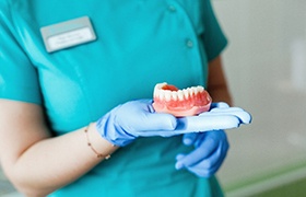 Closeup of dentist holding out dentures in Milton 