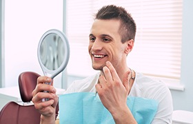 Man smiling while examining his tooth-colored fillings in Milton