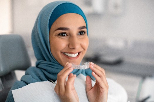 A woman holding an Invisalign aligner near East Milton