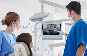 Dentist dental team member and patient looking at digital x-rays