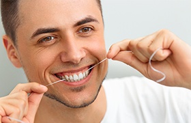 Man flossing teeth to maintain porcelain veneers