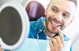 Man checking smile in mirror after teeth whitening in Milton, MA