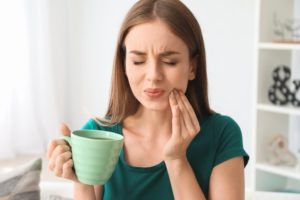 Woman holding mug with hand on face having a dental emergency